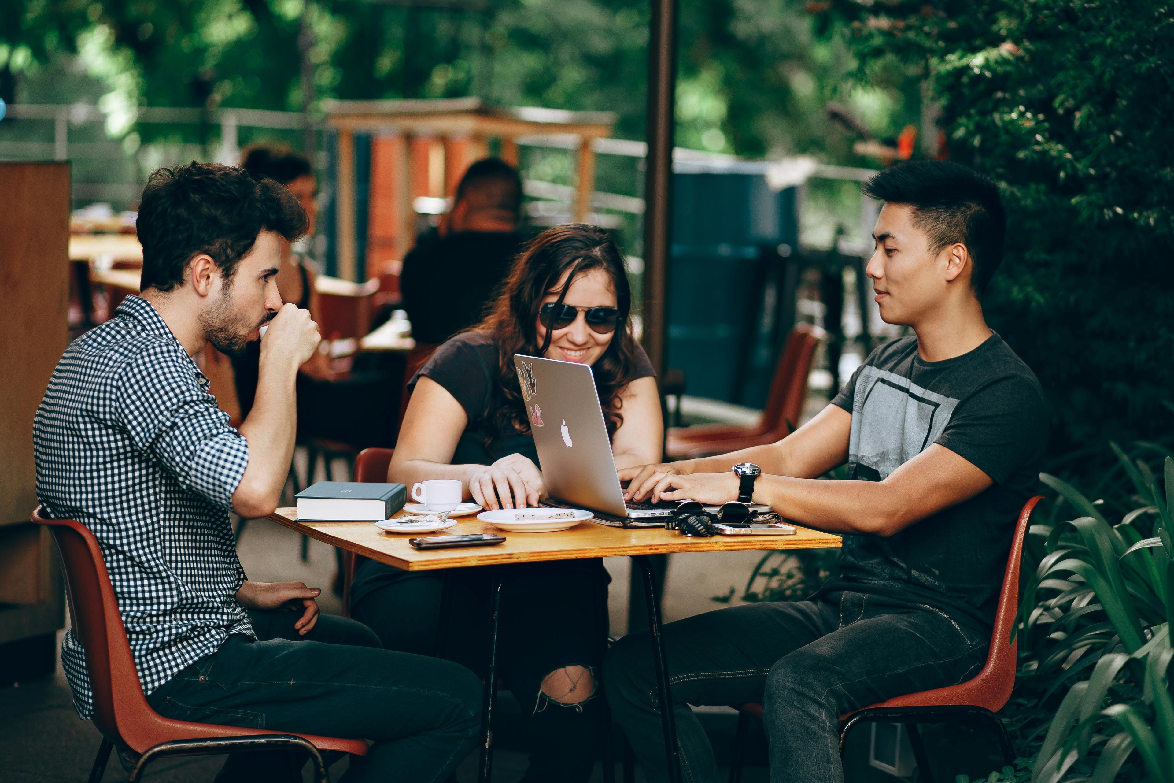 Three people looking at a laptop together at an outdoor cafe table